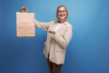 joyful 50s mature woman in jacket with s kraft shopping bag on studio background with copy space