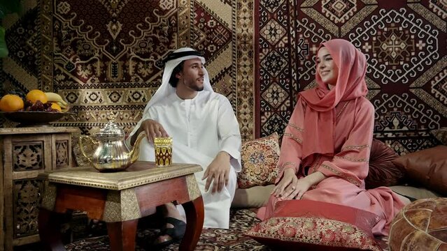 Middle eastern couple spending time together in an arab traditional house . Man with white kandura outfit and woman with colored abaya relaxing at home