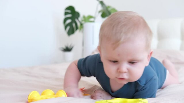 baby boy in blue bodysuit plays with colorful plastic rattle on bed