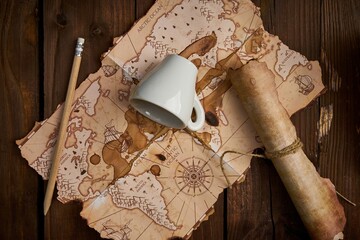 Aged parchment scroll with an old map and a spilled coffee cup on a wooden table.