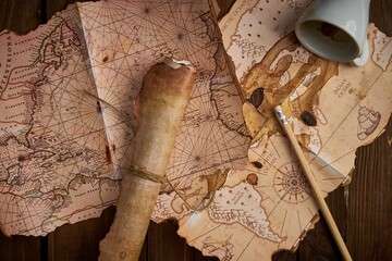 Antique parchment scroll with old maps and a spilled coffee cup on a wooden table.