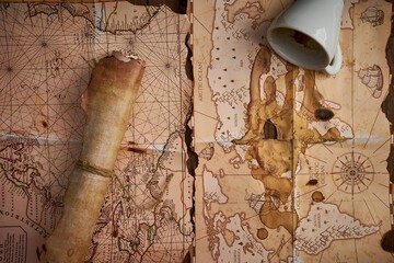 Antique parchment scroll with old maps and a spilled coffee cup on a wooden table.