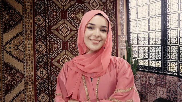 Beautiful young woman with pink colored abaya smiling at camera inside a traditional arab house. Concept about middle eastern cultures and lifestyles 