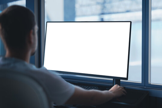 An engineer works on a computer with an empty blank screen - template, at an industrial company. In the background, there is a view of the production hall.