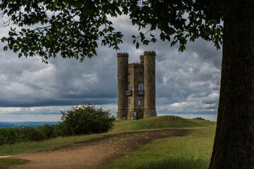 Tall stone tower is silhouetted against a cloudy sky on the green meadow