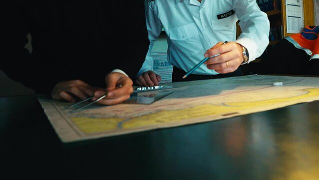 4K footage of planning a long trip on a freight ship. Captain and mate of ship is plotting navigation route on the map in the wheelhouse by using calipers, compass, set square and pencil stock video. - Powered by Adobe