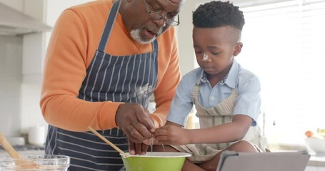 Happy african american grandfather and grandson having fun, baking in kitchen, slow motion