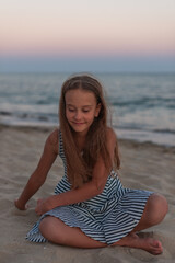 Fototapeta na wymiar a cute caucasian girl play on the beach on the sand and relaxes in casual striped clothing, 