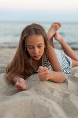 a cute caucasian girl play on the beach  on the sand and relaxes  in casual striped clothing, 