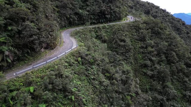 Drone footage over a road on hills between lush forest pn a sunny day