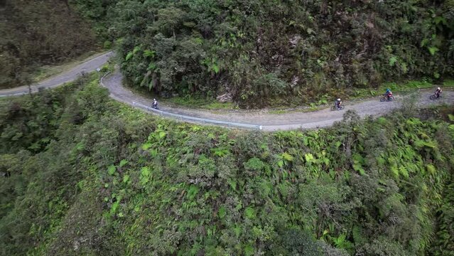 Drone footage over a road on hills between lush forest pn a sunny day
