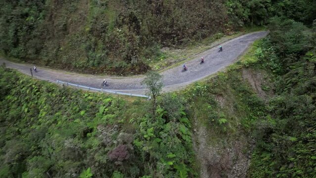 Drone footage over a road on hills between lush forest pn a sunny day