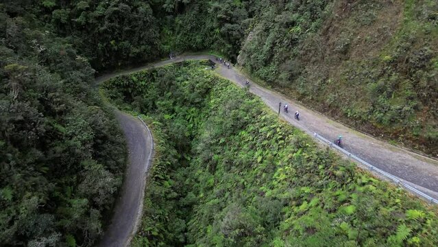 Drone footage over a road on hills between lush forest pn a sunny day