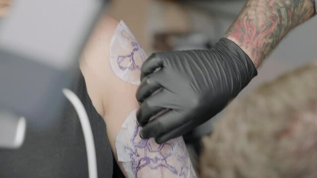 Caucasian Tattoo Artist making tattoo transfer paper on a female arm at a a tattoo salon