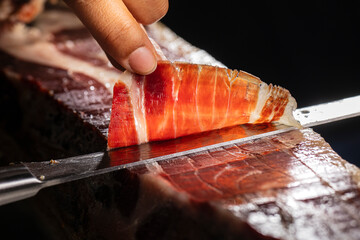 Jamón ibérico bellota Acorn-fed Iberian ham. Iberian ham cutter with knife making the best slice for tasting.  Jamón Ibérico ham cut with knife with selective focus and black background for copy space