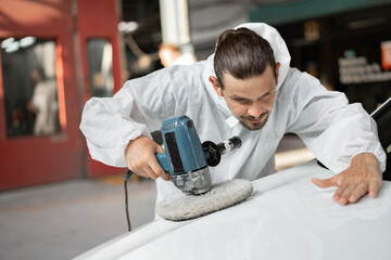 Caucasian man holds a polisher in the hand and polishes the car at car service