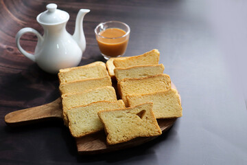 Fototapeta na wymiar Tea Time Snack. Healthy Wheat rusk served with Indian hot masala tea and milk jug over black background. also known as Mumbai cutting chai. with Copy space. Crunchy rusk or toast.