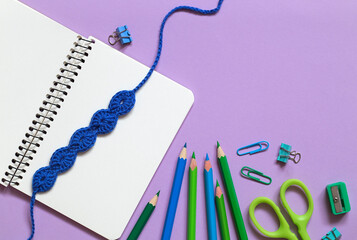 School stationery with blue crochet bookmark on a purple background. Top view. Copy space.