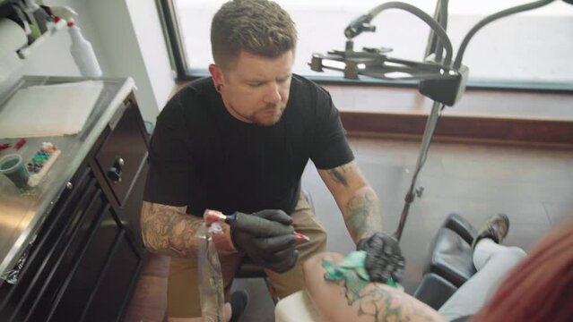 Professional Tattoo Artist making a tattoo on a red hair female arm at a salon