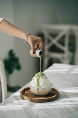 Vertical shot of a female's hand pouring green syrup on a delicious white dessert in a bowl