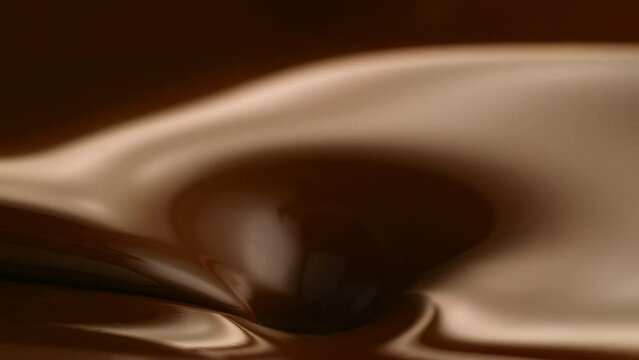 Slow motion of a hazelnuts falling into the brown melted chocolate