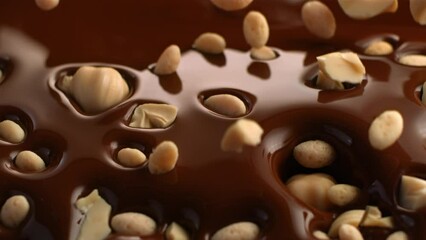Slow motion of small pieces of hazelnuts falling into the brown melted chocolate