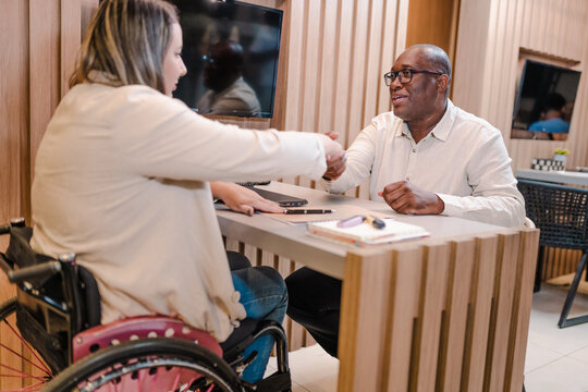 Brazilian woman in a wheelchair account manager at a bank in Brazil shaking her client's hand in a meeting about bank credit