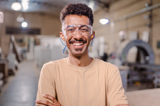 retrato de um homem afro Brasileiro professor de curso técnico de braços cruzados sorrindo para a câmera e usando óculo de proteção em um ambiente industrial