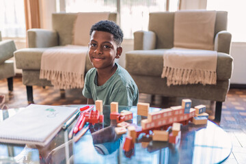 retrato de um menino negro Brasileiro pré adolescente sentado no chão da sala em sua casa no Brasil com brinquedos de montar na mesa