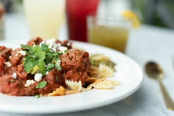 a white plate topped with meat and pasta with sauce and lemonade