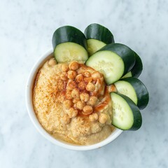 a white bowl with hummus and sliced cucumbers