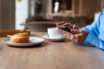 Woman having breakfast and using mobile phone. Female using phone in the coffee shop