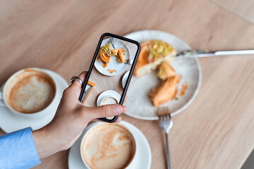 Hand holding mobile smart phone or cell telephone digital camera taking photo to cup of hot coffee and croissant. Food mobile photo concept