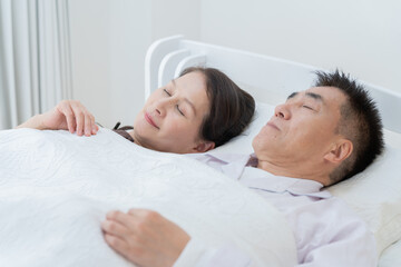 ベッドで眠る高齢者夫婦（睡眠・健康）