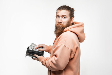 Fototapeta premium Handsom man holding paper currency in wallet and is unhappy on gray background. Hand pulling 100 dollars banknotes from wallet. Guy have cash. The concept of money, salary, finance, investment, save