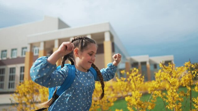 Girl child with backpack goes to school. Pupil for first time on an educational lesson. Happy little girl with backpacks runs to first lesson. The joy and smile of child. Concept of school education.