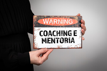 Coaching and Mentoring in Portuguese. A woman is holding a warning sign with text