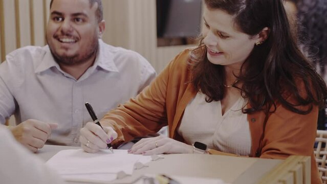detalhe ds um casal Brasileiro sorrindo assinando um contrato de financiamento bancario e apertando a mao do gerente do banco no Brasil