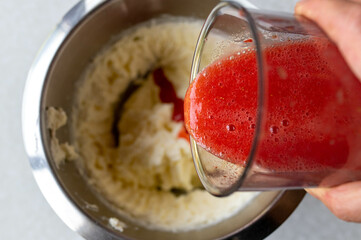 Pouring blended strawberries into a bowl with whipped cream for making strawberry cream 