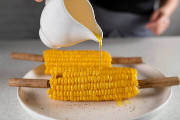 Pouring melted butter over corn on the cob