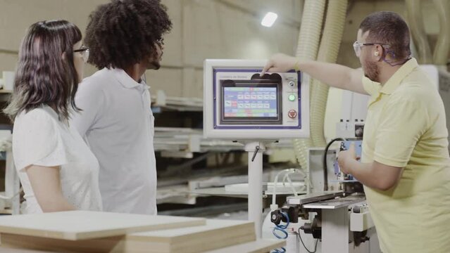 professor de um curso de tecnologia mostrando para os alunos como programar uma m&aacute;quina industrial durante aula pr&aacute;tica em uma f&aacute;brica no Brasil