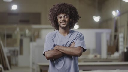 young Brazilian student with black power hair wearing safety glasses smiling at the camera and crossing his arms in a factory in Brazil