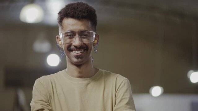 afro brazilian male technical course teacher with arms crossed smiling at camera and wearing goggles in an industrial setting