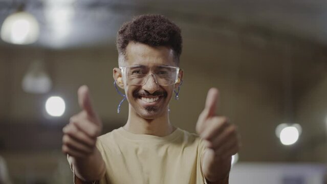 of an afro brazilian male technical course teacher wearing goggles and doing a positive sniff at the camera in an industrial setting
