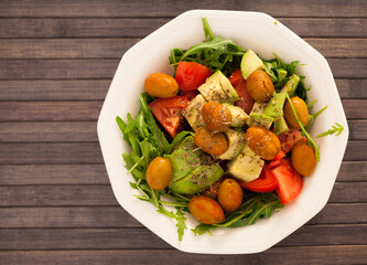 dish of fresh vegetables arugula, avocado, cherry tomatoes with olives on dining table