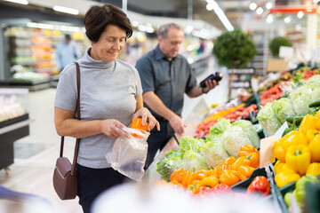 Smiling happy couple is choosing bell peppers and other vegetables in supermarket