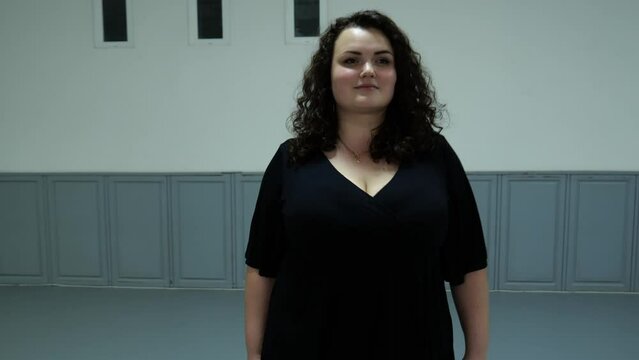 Portrait of a plus size model in dark clothes in a dance hall walking forward. Slow motion fat woman