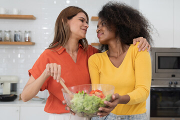Happy two young women embracing and cooking together in kitchen room at home. Two young diverse lesbian women spending time together at home. Diversity, LGBT and gender identity concept