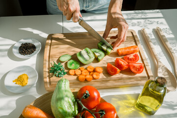 High angle of crop unrecognizable female cook cutting fresh kiwi on wooden chopping board while...