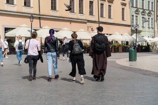 Authentic young priest in a black cassock walks with three teenage girls and backpacks along the street of the old European city of Krakow, a sunny summer day in city, multiculturalism and diversity